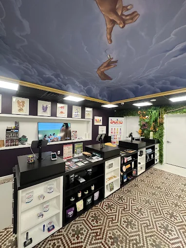 Inside The Hamm & Chaz dispensary in Jersey City — product counter beneath a hand-painted cloud ceiling mural